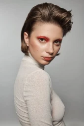 Portrait of a woman with short brown hair, red eye makeup, and a high-neck white top against a grey backdrop