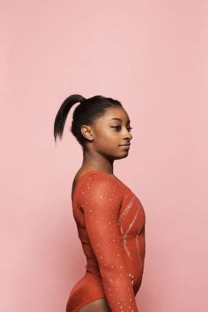 Portrait of Simone Biles in a red crystal-embellished leotard against a solid pink backdrop