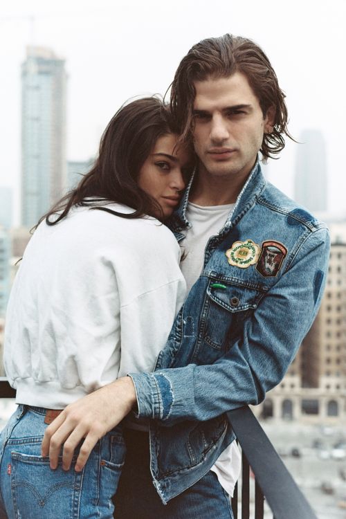 A young couple embraces in a denim and casual fashion shot against a city skyline background, showcasing a stylish, intimate moment.