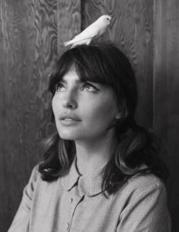 Black and white portrait of a woman wearing a collared dress with a small bird perched on her head by photographers Phil + Sara