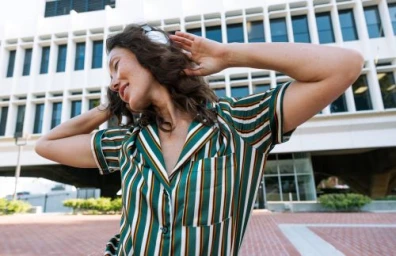 Woman in a green striped collared shirt wearing headphones against a modern building exterior.