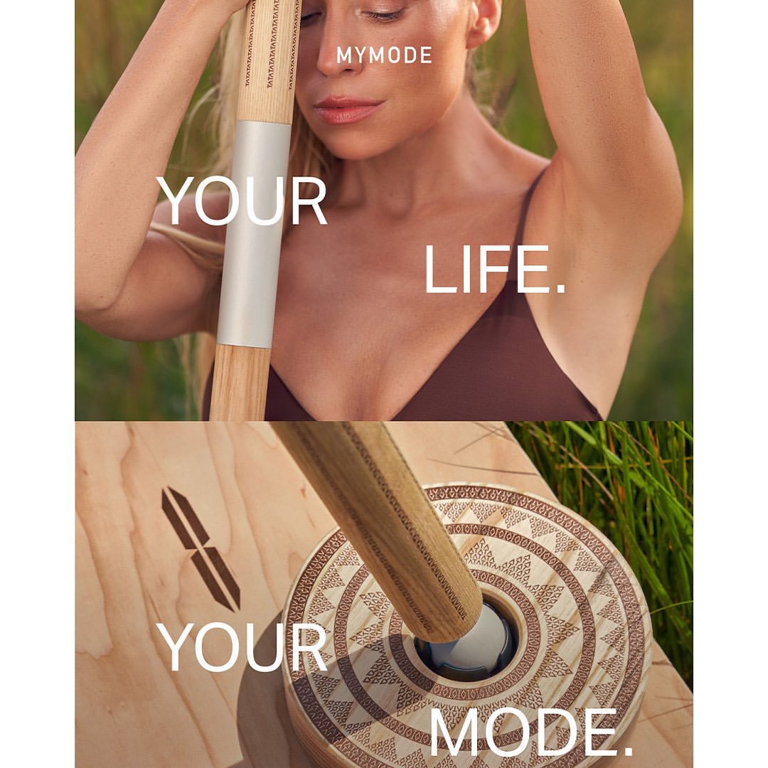 Woman with eyes closed and hands raised, alongside a wooden balance board and roller outdoors surrounded by green grass.