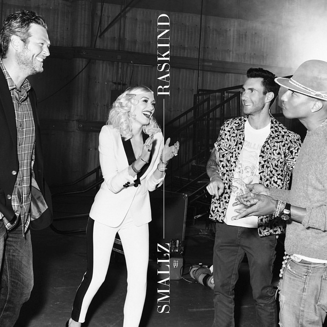 Black-and-white photo of Blake Shelton, Gwen Stefani, Adam Levine, and Pharrell Williams smiling in an indoor setting.
