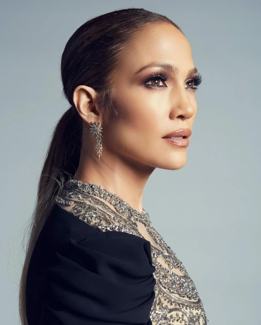 Portrait of Jennifer Lopez in a black dress with elaborate beaded detail, gazing off to the side against a grey gradient background.