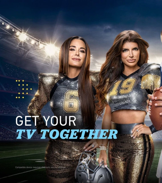 Two adult females wearing sports-themed apparel with football helmet, standing on a football field with stadium lights in the background.
