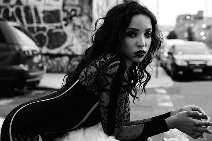 Black and white portrait of a woman in a dress with long wavy hair, leaning on a surface with cars and a graffiti wall background.