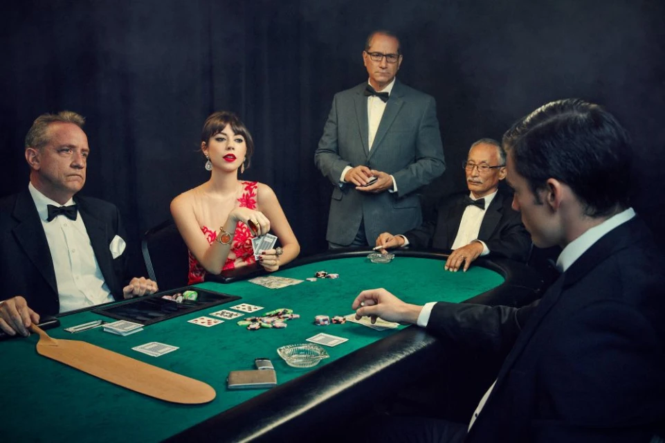 Group of people playing poker at a green felt table. Men and a woman in evening wear, formal attire, with cards and poker chips.