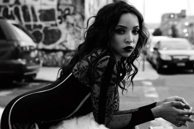 Monochrome portrait of a woman with dark wavy hair wearing a patterned lace sleeve dress outdoors on a city street.