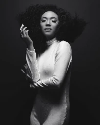 Monochrome portrait of a woman with voluminous dark curly hair wearing a white turtleneck and ring by Smallz + Raskind