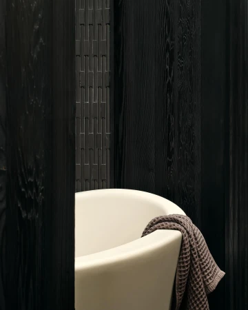 A cream-colored bathtub with a brown towel draped over the side, set against a backdrop of dark, vertical wood panels.