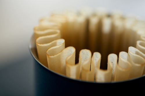 Close-up of fluted paper coffee filters inside a blue container, showcasing their texture and arrangement, against a blurred backdrop.