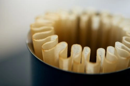 Close-up of fluted paper coffee filters inside a blue container, showcasing their texture and arrangement, against a blurred backdrop.