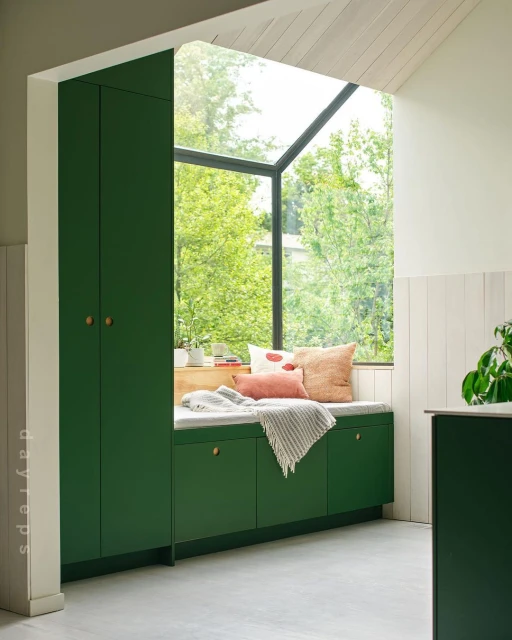 Bright and cozy window seat with green cabinetry, throw blanket, and pillows, creating an inviting indoor nook with natural light.