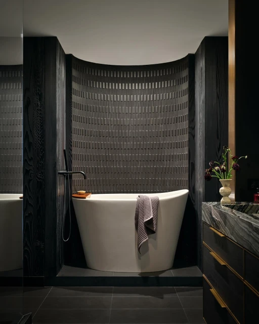 Modern bathroom features a white soaking tub with black wood wall panels and gray tile wall with black tile flooring indoors.