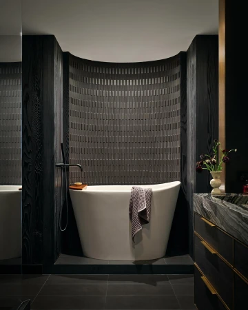 Modern bathroom features a white soaking tub with black wood wall panels and gray tile wall with black tile flooring indoors.