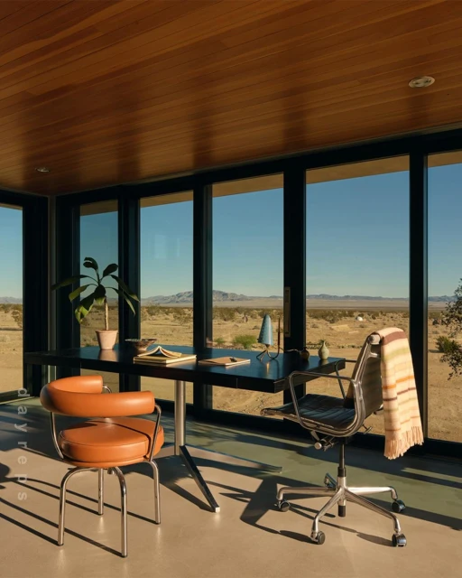 Home office with modern black desk and neutral-colored chairs in a room with large windows overlooking a desert landscape.