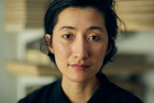 Close-up portrait of an Asian adult female with dark hair and a slight smile, soft lighting, and a blurred background indoors.