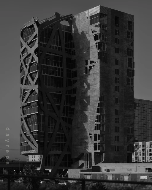 Monochrome architectural photograph of a tall modern building with a unique exterior framework, set against a clear sky in an urban environment.