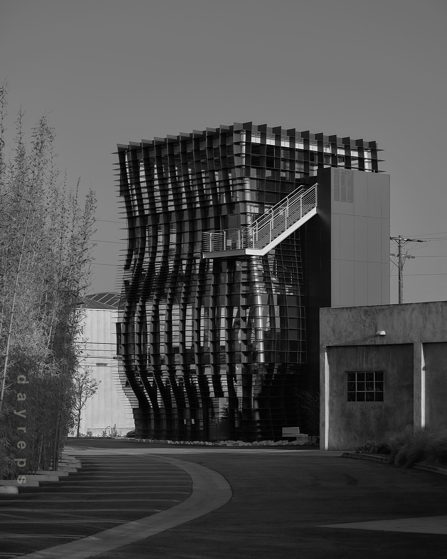 Modern architecture featuring an abstract geometric facade in black and white, next to an outdoor walkway with thin trees.