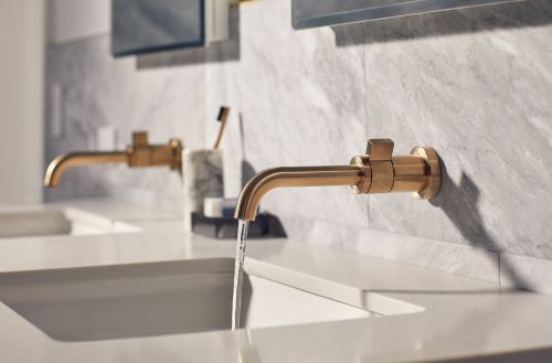 Close-up of a modern bathroom sink with a gold faucet and running water against a gray marble wall, creating a spa-like interior design.