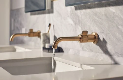 Close-up of a modern bathroom sink with a gold faucet and running water against a gray marble wall, creating a spa-like interior design.