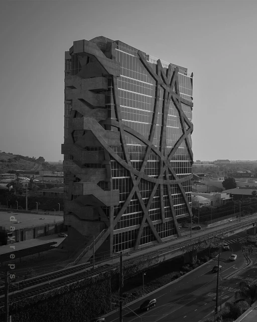 Black and white photo of a modern office building with a unique exterior design, concrete details, adjacent to a highway and train tracks.
