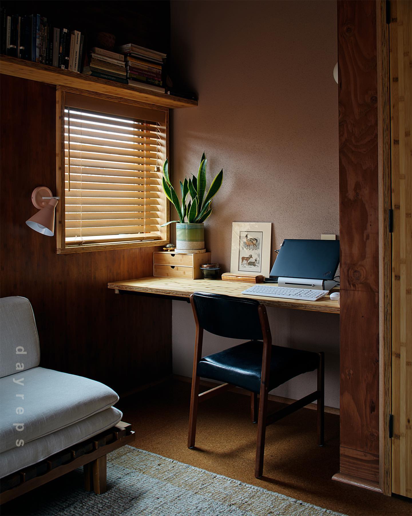 Indoor workspace featuring a wooden desk, chair, laptop, potted plant, and window with blinds creating a cozy and productive environment.