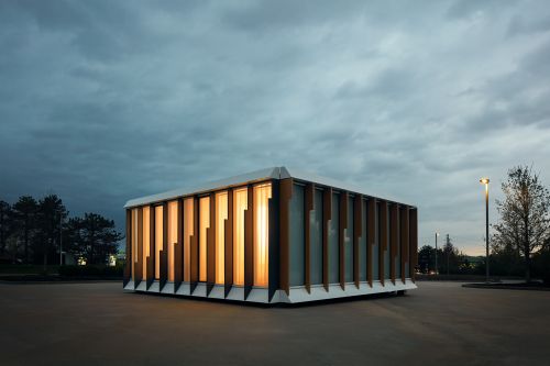 Modern architectural building with vertical slats glows warmly against an overcast sky and gray paved ground. Architectural design.