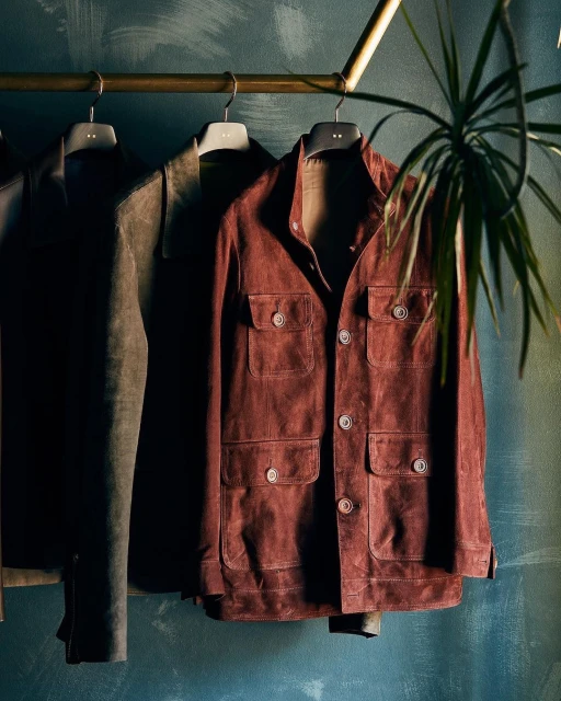 Hanging garments including a brown button-down jacket with pockets and other clothing on a metal rack with a houseplant.