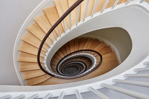 High-angle shot of a modern spiral staircase with wooden steps, white railings, and a dark brown handrail in an indoor setting.