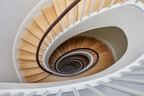 High-angle shot of a modern spiral staircase with wooden steps, white railings, and a dark brown handrail in an indoor setting.