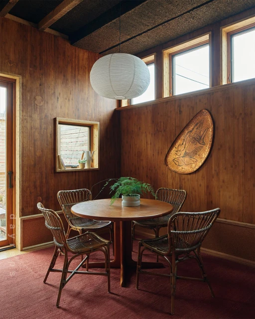 Cozy mid-century modern dining room with wooden walls, round table, and wicker chairs, illuminated by a hanging paper lantern.