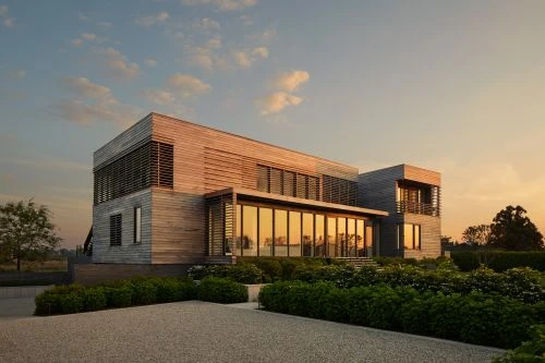 Exterior of a modern, wood-clad house with large windows and manicured landscaping at sunset, reflecting a serene architectural design.