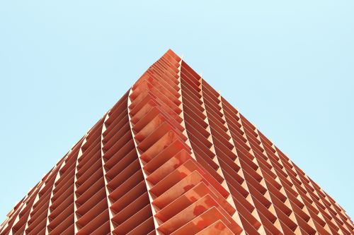 Angular, terracotta-colored architectural facade with geometric patterns against a clear blue sky in warm, natural lighting.