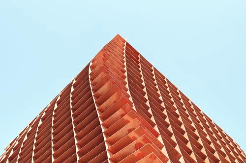 Angular, terracotta-colored architectural facade with geometric patterns against a clear blue sky in warm, natural lighting.