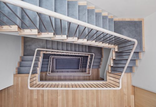Top-down view of a modern staircase with gray carpet steps and a white handrail, showcasing architectural design and interior detail.