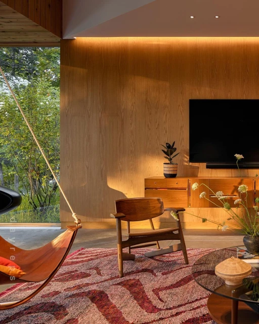 A stylish interior showcasing a leather sling chair, wooden accent chair, patterned rug, and wooden furniture against a backdrop of natural light.