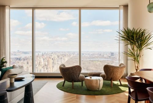 Bright modern interior with large windows overlooking a cityscape, featuring stylish chairs, a sofa, and natural light in a neutral palette.