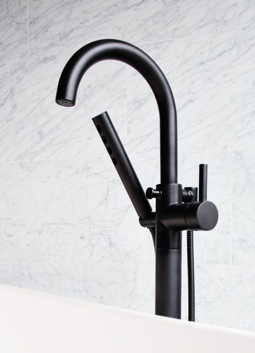 Close-up of a sleek, matte-black freestanding faucet with a handheld sprayer next to a white bathtub and marble tile wall, showcasing modern bathroom design.