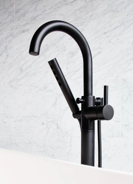 Close-up of a sleek, matte-black freestanding faucet with a handheld sprayer next to a white bathtub and marble tile wall, showcasing modern bathroom design.