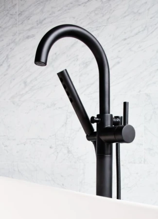 Close-up of a sleek, matte-black freestanding faucet with a handheld sprayer next to a white bathtub and marble tile wall, showcasing modern bathroom design.