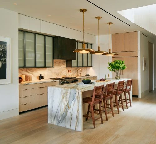 Bright, modern kitchen interior featuring a marble waterfall island, wooden barstools, and stylish pendant lighting for an elegant design.