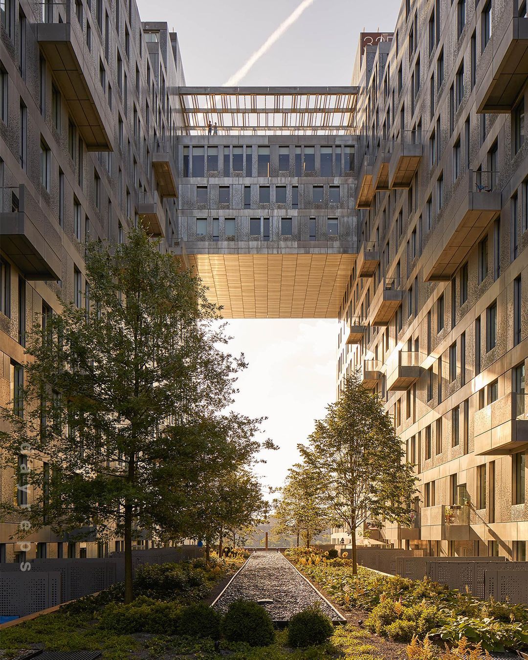 Exterior view of contemporary brick buildings connected by enclosed walkways above a landscaped courtyard with trees and pathways.