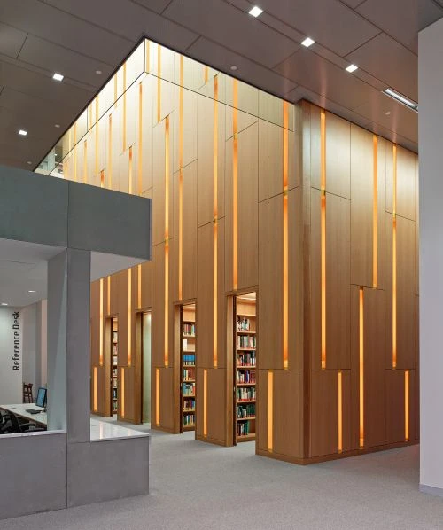 Modern library interior featuring light wood paneling with integrated vertical lights, creating a warm, inviting atmosphere with bookshelves.