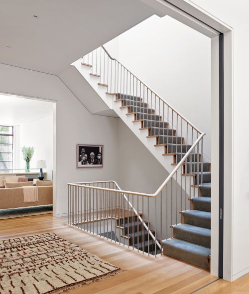 Interior view of a modern home featuring a staircase with metal railings, light hardwood floors, and a minimalist design aesthetic.