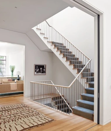Interior view of a modern home featuring a staircase with metal railings, light hardwood floors, and a minimalist design aesthetic.