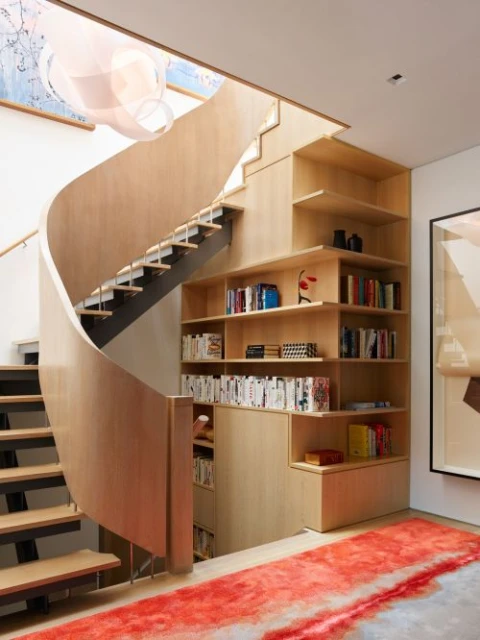 Interior view of a modern home featuring a unique spiral staircase with integrated wooden bookshelf, accentuated by a red and white rug.