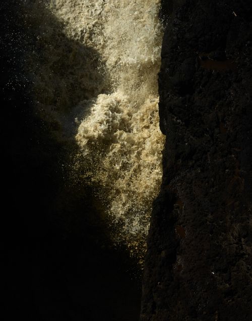 Close-up of a powerful waterfall cascading down dark rocks, water and stone creating a dynamic, natural scene in contrasting light.