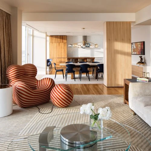 Living room interior with a modern red and white striped chair, a glass coffee table, and a dining table with blue chairs in the background.
