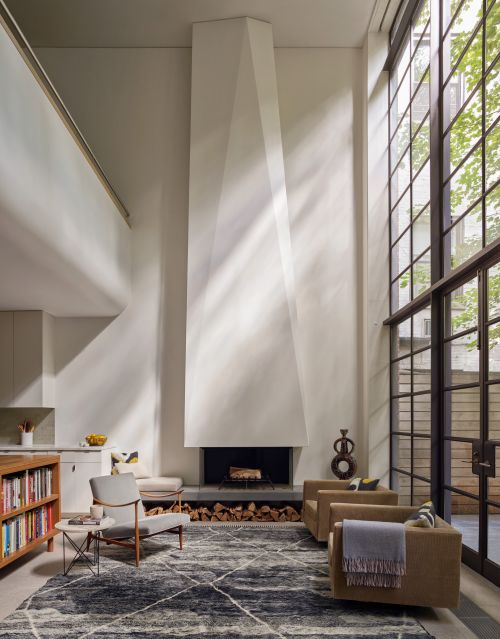 Living room interior featuring modern fireplace, armchairs, area rug, and natural light from large windows in a minimalist setting.